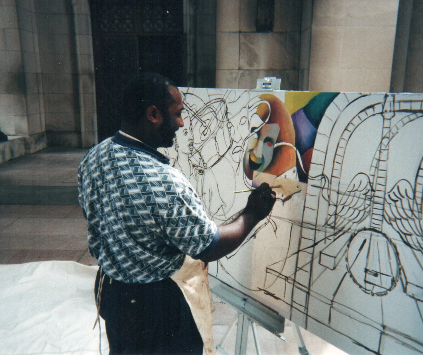 Michael McBride is an African American man. He is pictured here in a green and white patterned shirt, facing away from the camera, working on a painting.